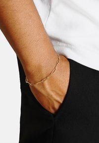Bracciale in oro con maglie allungate, indossato su un polso. Il tono della pelle rende visibile la texture, con un design semplice.