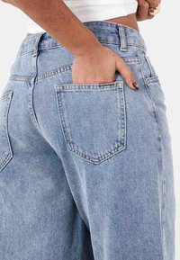 Jeans de mezclilla azul claro de cintura alta con un corte relajado, que cuentan con un bolsillo trasero y detalles de costura sutiles.