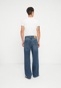 Blå vide jeans laget av denim, med en brun lærlapp på baksiden, to baklommer og en standard glidelås.