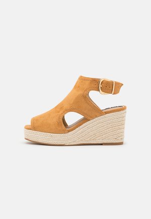 Sandały na koturnie z jasnobrązowego zamszu, otwarty przód z wycięciami, regulowany pasek na kostkę oraz teksturowana podeszwa z juty.
