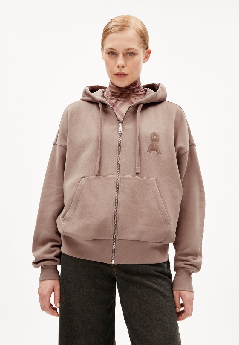 Sweat à capuche zippé marron avec une poche avant, un capuchon réglable par cordon, et un logo brodé sur la poitrine. Tissu doux et texturé.