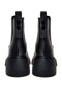 Botines negros de cuero, con un upper texturizado, punta redonda, suela de plataforma gruesa y dos botones decorativos negros en la parte trasera.