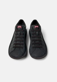 Sneaker in suede nero con profilo basso, dotate di sei lacci neri e logo rosso "CAMPER" sulla linguetta. Texture liscia e design della punta arrotondata.