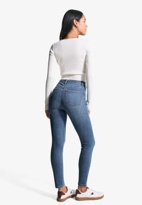 Valkoinen ribattu pitkähihaine paita yhdistetty tummansiniset tiukat farkut, joissa on korkea vyötärö ja takataskut. Asusteena valkoiset tennarit ruskeilla yksityiskohdilla.