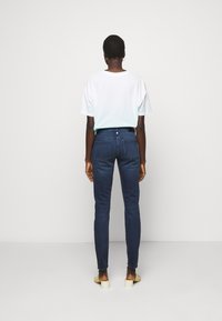 Donkerblauwe skinny jeans, hoog in de taille met zakken, gecombineerd met een wit T-shirt met een subtiele verloop van wit naar lichtblauw.