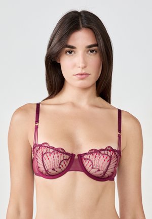 Bralette en dentelle bourgogne avec bordure festonnée, bonnets transparents et design floral brodé contrastant. Bretelles réglables avec accents dorés.