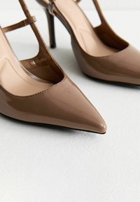 Chaussures à talon haut en cuir verni beige avec un bout pointu et une sangle de cheville. Texture lisse avec une finition brillante, dotées d'un talon fin.