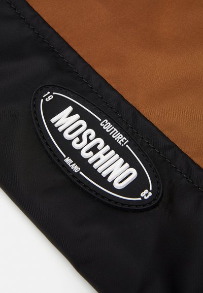 Moschino patch on brown and black synthetic fabric, featuring a prominent oval logo with "COUTURE!" and "MILANO" text in white.
