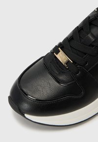Baskets en cuir noir avec surface texturée, dotées de lacets noirs, de quincaillerie dorée et d'une semelle blanche avec des détails accentués en noir.