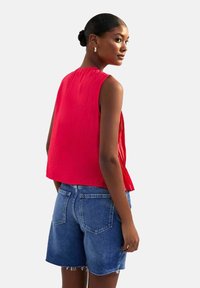 Haut sans manches rouge avec une coupe ample, en tissu texturé, ourlet arrondi, associé à un short en denim bleu avec des bords effilochés et des poches arrière.