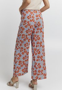 Vida byxor i ljusblått tyg med ett blommönster i röd och beige. Elastisk midja och slät textur. Klacksandaler med blockhäll bärs.