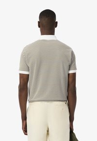 Randig polo skjorta i kräm och brunt med vit krage. Kort ärm, textil med struktur och avslappnad passform. Sedd bakifrån.