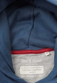 Marinblå hoodie med röd accent på insidan. Lappen säger "Band of Rascals", 100% ekologisk bomull, storlek 140, med skötselråd på flera språk.