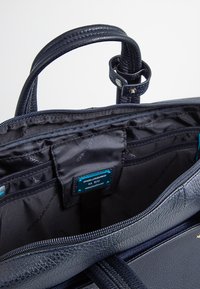 Borsa a mano in pelle blu navy con superficie texturizzata; l'interno presenta una fodera in tessuto nero, molteplici tasche e una chiusura con zip.