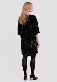 Green sequin dress with short sleeves, loose fit, round neckline, and mid-thigh length, paired with black tights and heels.