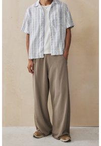 Koszula w paski z krótkim rękawem w kolorze niebieskim i białym, zestawiona z beżowymi spodniami o szerokich nogawkach. Casualowe buty z teksturowaną podeszwą dopełniają wygląd.