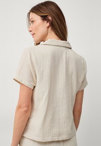 Beige kortebloes met een textuur in de stof, voorzien van een kraag en een subtiel ruitpatroon, met opgerolde mouwen en een losse pasvorm.