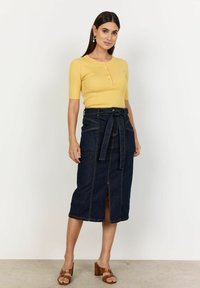 Gul ribbad kortärmad topp med knappar, tillsammans med en högmidjad mörk denimkjol med knytband och framtida slits. Bruna klacksandaler.