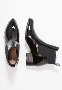 Bottines en cuir verni noir avec bout pointu, panneaux latéraux élastiques et petit talon carré. Texture lisse avec une finition brillante.