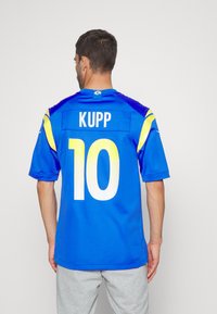Blå kortermet trøye med gule detaljer, som har navnet "KUPP" og nummer "10" på baksiden. Glatt tekstur, atletisk passform.