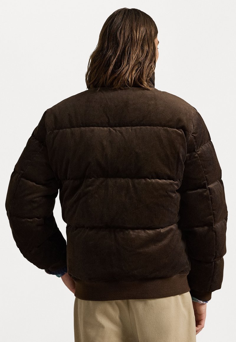 Veste matelassée en velours côtelé marron avec rembourrage horizontal et poignets côtelés. Elle dispose d'un col montant et d'un ourlet élastiqué pour plus de chaleur.