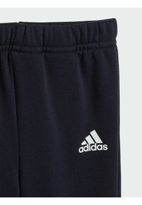 Pantaloni sportivi blu navy con tessuto testurizzato, dotati di un elastico in vita e un logo Adidas bianco sulla parte bassa della gamba.
