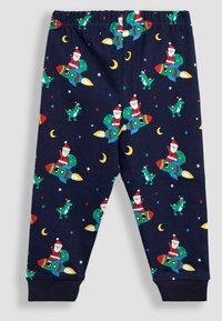 Pantalones de pijama azul marino de algodón, con un diseño de Santa Claus en cohetes y dinosaurios, adornados con lunas y estrellas en colores brillantes.
