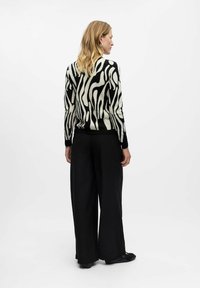 Un pull rayé noir et blanc à manches longues, associé à un pantalon large noir et des chaussures noires plates. Le matériau en tricot texturé est visible.
