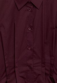 Buttoned deep burgundy shirt with pointed collar and visible stitching details.