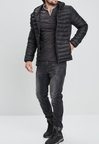 Giacca a vento nera con cappuccio, indossata sopra una maglietta a maniche lunghe grigia scura. Jeans in denim e stivali neri completano l'outfit. Materiali texture visibili.