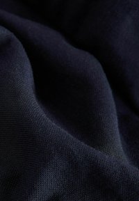 Tmavě modrá látka zblízka, texturovaná vazba, měkký pád s viditelnými vlákny, hladký povrch s jemným leskem.