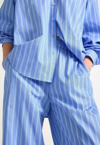 Blå stribet skjorte og matchende bukser, lavet af glat stof. Skjorten har en knaplukning og en løs, oversized pasform. Bukserne har en elastisk talje.