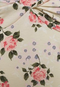 Tissu à motif floral présentant de grandes roses roses et de petites fleurs violettes sur un fond beige clair, avec des feuilles vertes. Matière douce et texturée.