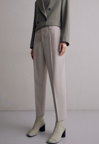 Olivově zelený dvouřadý blejzr v kombinaci s béžovými upravenými kalhotami, doplněný světle zelenými lodičkami na vysokém podpatku a odpovídajícími ponožkami.