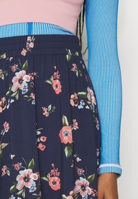 Maglietta a maniche lunghe a righe blu e bianche abbinata a una gonna floreale blu marina con fiori rosa e bianchi e una vita elasticizzata.