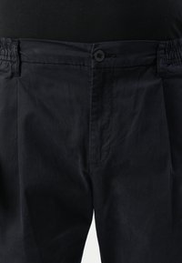 Pantaloni blu navy con elastico in vita, chiusura a bottone e due tasche laterali. Presentano una superficie liscia e un design rilassato.