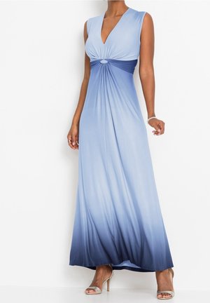 Donna che indossa un abito lungo senza maniche blu sfumato con scollo a V e dettaglio arricciato in vita, abbinato a sandali beige con tacco alto e braccialetto.