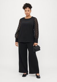Czarna bluzka z przezroczystymi balonowymi rękawami w groszki, zestawiona z szerokimi czarnymi spodniami. Dodatki to mała czarna torebka i baleriny.