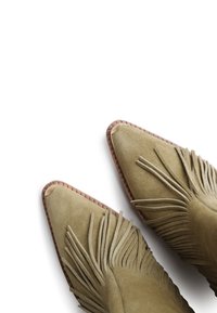 Bottes à cheville en daim vert avec des détails en franges, orteils pointus et une semelle marron cousue. Texture lisse avec des accents de franges visibles.