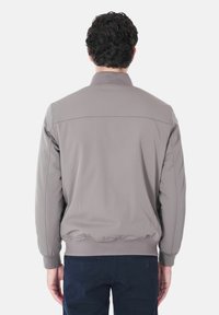 Giacca zip-up grigia chiara con colletto alto, polsini ed orlo elastici, e dettagli di cucitura sottili sul retro. Texture liscia e design aderente.