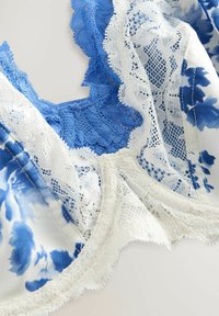 Soutien-gorge léger avec un tissu à motif floral bleu, orné de dentelle blanche et de bords festonnés, mettant en valeur des détails dentelés et une texture raffinée.