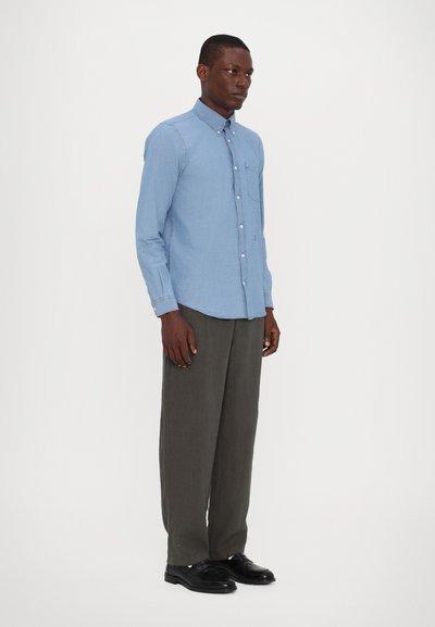 Light blue button-up shirt with long sleeves, a chest pocket, and a rounded hem, paired with dark grey trousers and black shoes.