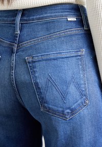 Blå denimjeans med høy midje, kontrasterende sømmer og en baklomme med et distinkt chevronmønster.