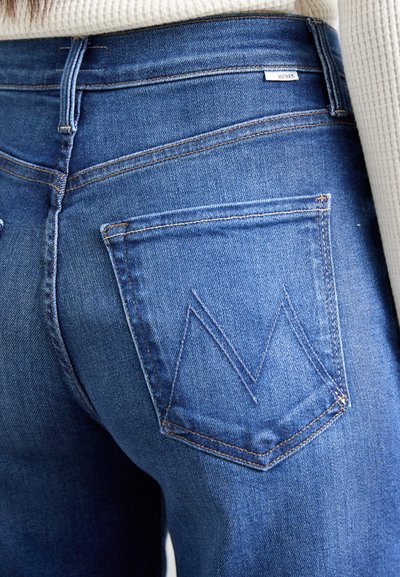 Blue denim jeans featuring a high waist, contrasting stitching, and a back pocket with a distinct chevron pattern.