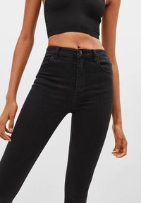 Jeans negros de cintura alta y ajuste slim, fabricados en denim suave. Cuenta con cinco bolsillos, pasadores para cinturón y un cierre frontal con botón.