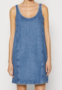 Denim-asu pyöreällä kaula-aukolla ja ilman hihoja. Vaaleansininen väri, suora malli ja näkyvä ommel saumoissa.
