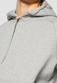 Gros plan sur une personne portant un sweat à capuche gris clair avec un cordon noué en un simple nœud.