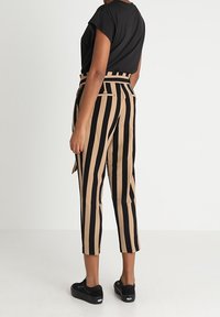 Zwart en beige gestreepte broek met een hoge taille, taps toelopende benen en zijzakken, gecombineerd met een zwart top met korte mouwen en zwarte schoenen.