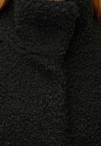 Sort fleecejakke med høj krave, tekstureret stof og et hyggeligt udseende. Detaljerne inkluderer en blød, let fluffy overflade.