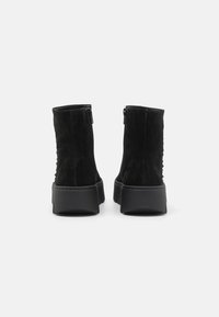 Bottines en suède noir avec une semelle plate noire et des fermetures éclairs sur le côté, présentant des détails texturés le long de l'arrière.